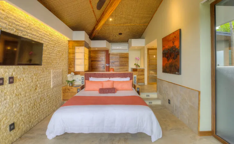 Tropical modern bedroom design featuring a king bed with terracotta bedding, rough stone accent wall, and woven ceiling