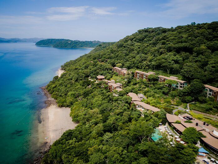 Aerial view of secluded luxury resort with villas nestled in lush greenery along a pristine beachfront