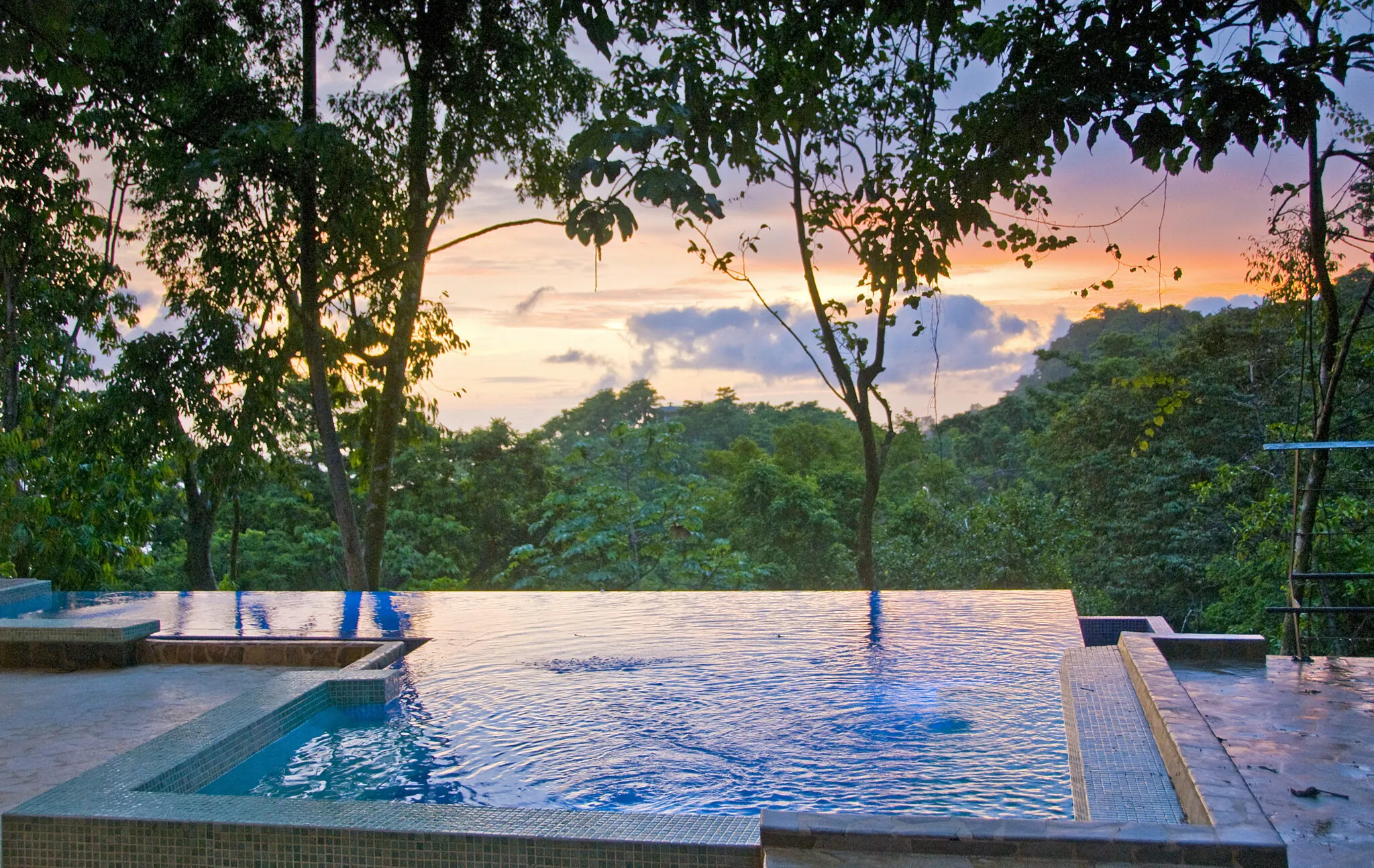 Infinity pool at sunset with a view of a lush tropical forest.